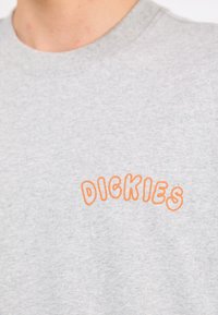 Gray sweatshirt with ribbed crew neck, featuring orange embroidered "DICKIES" logo on the left chest. Fabric appears soft and textured.