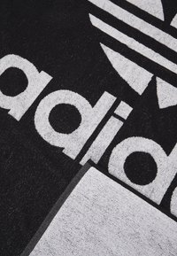 Toalla negra con un destacado logo blanco de Adidas y diseño de tres franjas. Textura suave con un detalle de borde negro en la parte inferior.