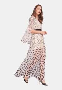 Abito lungo e trasparente a pois beige con macchie nere e una cintura nera in vita, caratterizzato da maniche larghe e una silhouette fluida. Sandali neri con tacco.