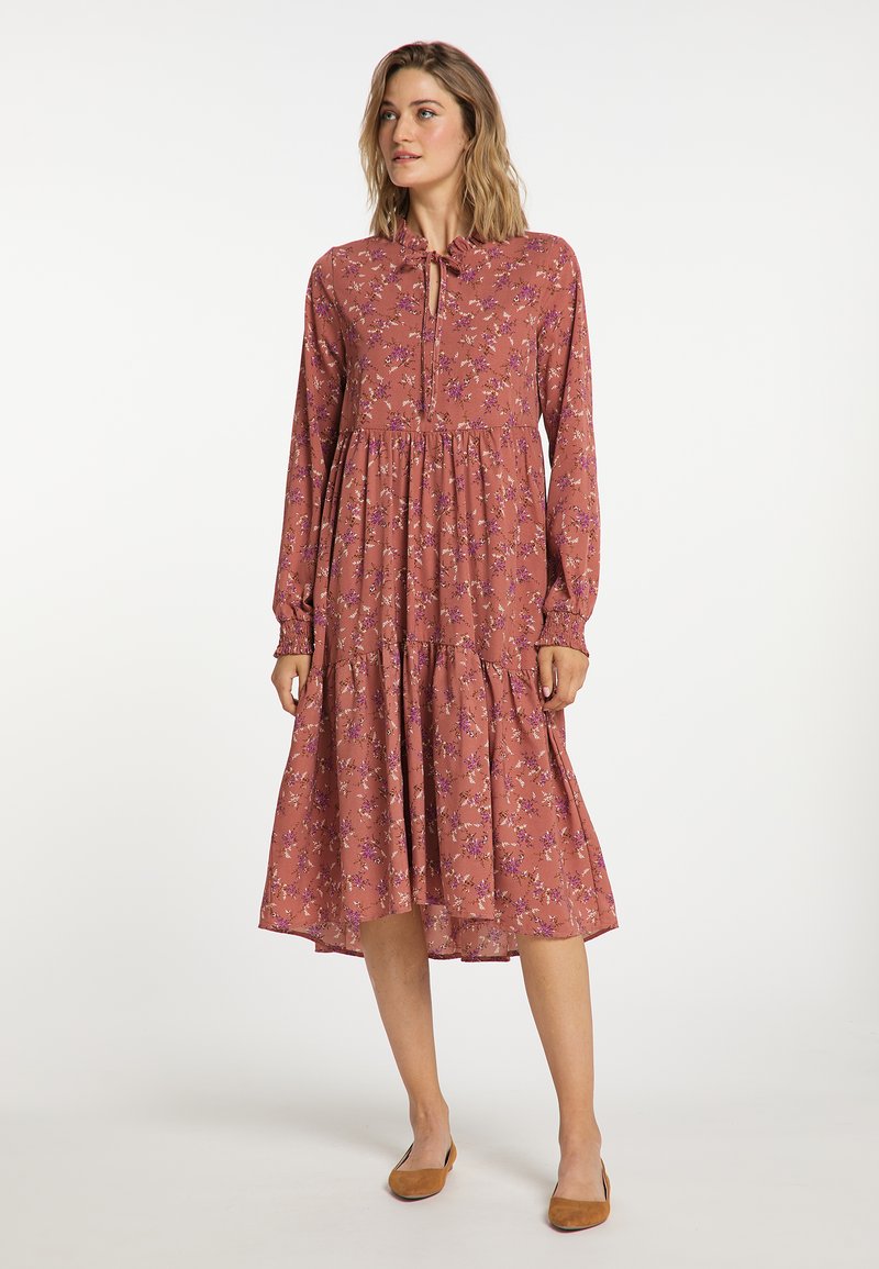 Rochie roz, cu mâneci lungi, cu fustă de tip tiered, model floral și decolteu fetiță. Include o deschidere în formă de cheie în față și manșete.