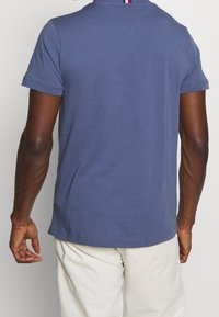 Modré bavlněné tričko s krátkým rukávem, s kulatým výstřihem a přímým lemem. Na zádech má vertikální barevný akcent v červené a bílé.