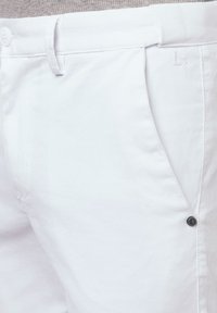 Białe spodnie bawełniane z domieszką, o gładkiej fakturze, z zapięciem na guzik, kieszeniami bocznymi oraz subtelnym wytłoczonym logo na materiale.