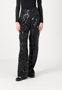 Pantaloni neri in paillettes con una vestibilità rilassata, caratterizzati da strisce verticali e una superficie testurizzata. Tessuto liscio con riflessi lucidi.