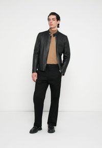 Crna kožna jakna sa uspravnim ovratnikom, nošena preko smeđeg džempera. Uparena s crnim hlačama i tamnim cipelama, karakterizira je uski kroj.