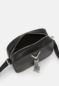 Black leather crossbody bag with a textured finish, silver hardware, zip closure, and a tassel detail. Compact rectangular shape.