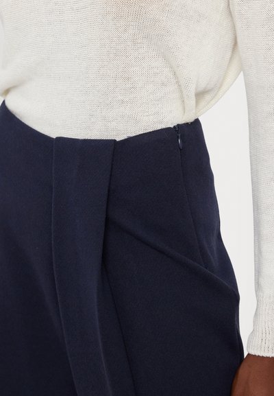 Mørkeblå skreddersydde bukser med høy midje, plissert front, glidelås og mykt teksturert stoff, kombinert med en lett strikket topp.