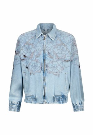 Veste en denim bleu clair avec fermeture éclair sur le devant, poignets et ourlet élastiques, présentant des motifs complexes de découpe en dentelle florale sur la poitrine et les manches.