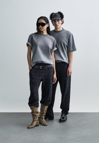Gray t-shirts with rolled sleeves, black patterned pants, and textured boots. Accessories include dark sunglasses and a black fur-trimmed cap.