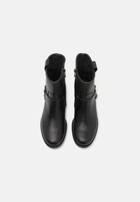 Botas de cuero negro hasta el tobillo con un acabado suave, que cuentan con un zipper en el costado, un detalle de correa y un diseño de puntera redondeada.
