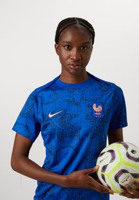 Blue Nike soccer shirt with a patterned design, featuring an orange rooster logo and crew neckline, held with a multi-colored soccer ball.