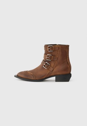 Botas de cuero marrón hasta el tobillo con tres hebillas plateadas, punta afilada y costuras decorativas a lo largo de los lados. Tacón bajo en bloque.