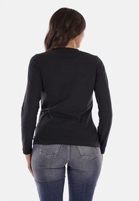 Maglietta nera a maniche lunghe con scollatura rotonda, realizzata in tessuto morbido. La persona indossa jeans blu, che mostrano una silhouette aderente.