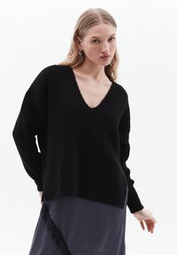Maglione nero lavorato a maglia con scollatura a V profonda, maniche lunghe e vestibilità ampia; presenta un motivo texturizzato e polsini a coste.
