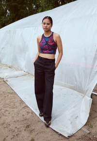 Sorte høye bukser kombinert med en tettsittende, flerfarget crop topp med blomster- og geometriske mønstre. Modellen står sikkert utendørs.