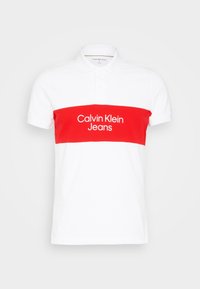 Biała koszulka polo z czerwoną poziomą linią i napisem „Calvin Klein Jeans”. Wykonana z bawełny, z klasycznym kołnierzykiem i krótkimi rękawami.