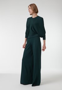 Groene geribbelde top met gedrapeerd detail, gecombineerd met wijde broek in bijpassende stof. Soepele textuur, aansluitend rond de taille en een relaxte pasvorm.