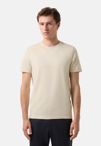 Cremefarvet bomulds t-shirt med rund hals og korte ærmer. Har et diskret præget logo på brystet. Glat tekstur, afslappet pasform.