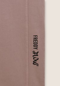 Tela de color rosa claro con una textura suave, que presenta texto impreso en negro "FREDDY" y "flow" a lo largo de la costura lateral. Diseño sencillo y moderno.