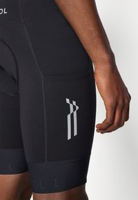Shorts de cyclisme noirs présentant une coupe ajustée, un matériau lisse, des accents réfléchissants et un logo près de la ceinture et de la cuisse.