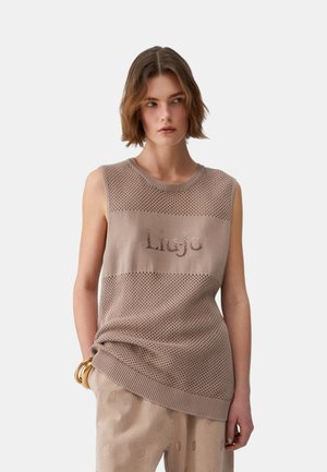 Giovane donna con capelli corti castani che indossa un top beige senza maniche in maglia con il logo "Liu Jo" e pantaloni beige abbinati con motivo.