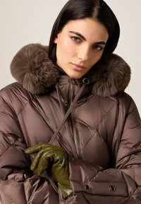 Braune gesteppte Jacke mit Kunstpelzkragen, die ein diamantförmiges Steppmuster aufweist, und grüne Lederhandschuhe mit engem Schnitt.