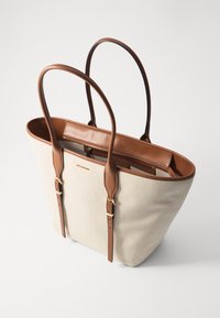 Borsa tote in tela color beige chiaro con dettagli e manici in pelle marrone. Presenta una tasca interna con zip e spallacci regolabili.