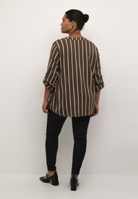 Brown and cream striped shirt with rolled sleeves, rounded hem, paired with black skinny pants and black heels. Smooth fabric texture.