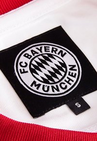 FC Bayern München shirtlabel met een zwarte, ronde patch met witte borduursels, die een diamanten patroon en de teamnaam weergeeft. Rood en witte kleuren.