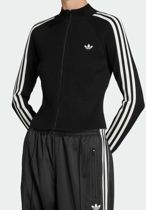 Veste de sport noire zippée avec des détails à trois bandes blanches sur les manches et pantalon noir assorti avec des bandes blanches et des logos.