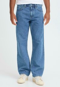 Lyseblå denimjeans med løs passform, rette ben og synlige sømmer. Brukes med kremfargede sneakers med klassisk design.