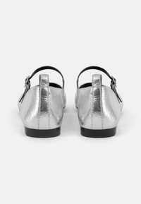 Silver ballet flats with a smooth metallic finish, back strap, small buckle, and a rounded toe design. Flat black sole and minimal detailing.
