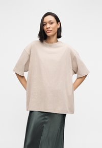 Μπεζ αθλητική μπλούζα σε μεγάλο μέγεθος με κοντά μανίκια, στρογγυλή λαιμόκοψη και απαλή υφή, συνδυασμένη με σκούρο πράσινη σατέν φούστα.