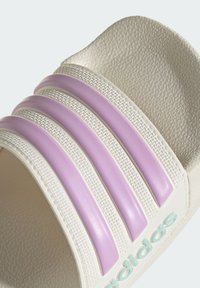 White slide sandal featuring three horizontal lavender stripes, textured surface, and a blue logo on the side. Designed for casual wear.