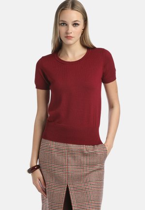 Rød kortærmet striktop med rund halsudskæring, ribbet kant og glat tekstur, parret med en ternet nederdel med en slids over knæet.