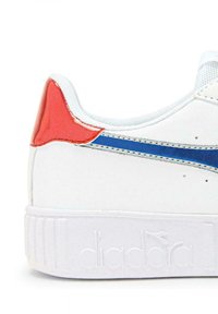 Sneaker bianco con un accentuato tallone rosso lucido, striscia blu e suola bianca texture. Presenta un materiale liscio e un branding in rilievo.