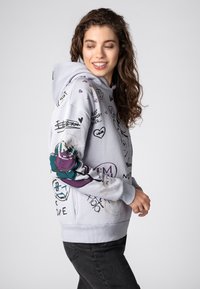 Lichtgrijze hoodie met diverse grafische ontwerpen, waaronder harten en glimlachende gezichten, met een opvallend bloemmotief op de mouw.