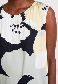 Top senza maniche con motivo floreale che presenta tonalità di nero, beige e verde chiaro. Tessuto morbido con scollatura rotonda e dettagli arricciati.