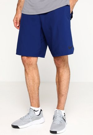 Shorts de sport bleu marine en tissu léger, avec un logo Nike noir sur la jambe gauche, associés à des baskets grises.