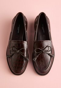 Mocasini maro închis din piele cu un model texturat de crocodil, prevăzuți cu o fundă și detalii cu ciucuri în față și un design cu vârf rotunjit.