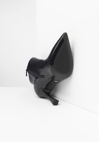 Botte noire en cuir à talons hauts avec un bout pointu, fermeture éclair sur le côté et semelle texturée. Présente un talon aiguille mince et un design minimaliste.