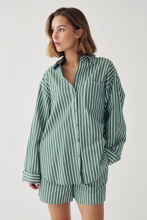 Ung kvinde iført en løs langærmet skjorte med grønne og hvide lodrette striber og matchende shorts, som kigger mod sin venstre side.