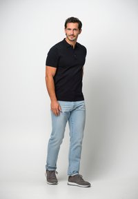 Marinblå kortärmad polo, ljusblå jeans och grå sneakers. Modellen har en avslappnad hållning, utan märkbara mönster eller texturer.