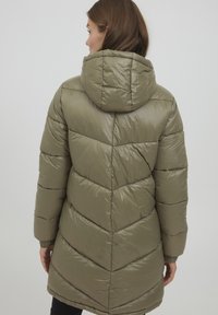 Manteau en duvet vert olive avec capuche, présentant un design matelassé en chevrons, des poignets élastiques et une texture lisse et brillante.