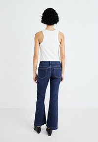 Jeans svasati blu scuro con vita alta, due tasche posteriori e dettagli di cucitura sottili, abbinati a un top a canotta bianco aderente.