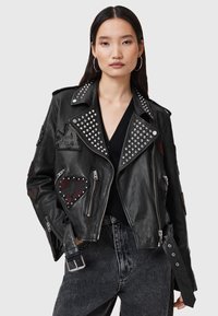 Black leather biker jacket featuring silver studs, patches, and zippers. Includes a belted waist and textured finish.