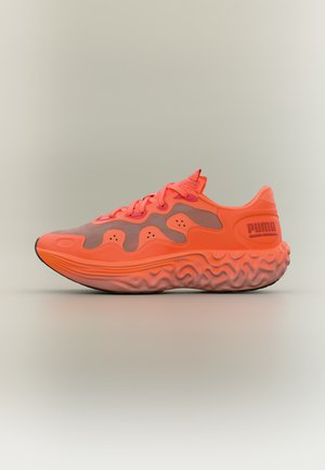 Fel oranje Puma sneaker met gestructureerde zool en golfachtige designpatronen aan de zijkant, getoond in profiel op een neutrale achtergrond.