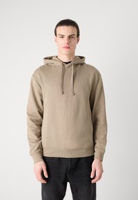 Felpa beige con cappuccio regolabile, polsini ribattuti e orlo. Presenta un marchio discreto sulla parte anteriore. Il materiale sembra morbido e liscio.