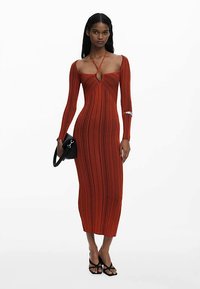 Punane soonikkangast midi-kleit pikkade varrukatega, millel on kaeluse juures võtmeaugu detail ja keha järgnev lõige. Käe peal must käekott.