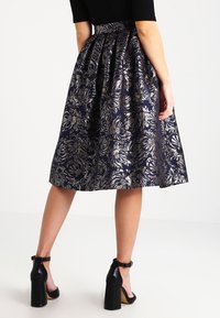 Rozšířená midi sukně z navy modré látky s metalickým květinovým vzorem. Elastický pas a hladká textura, spárovaná s masivními černými podpatky.
