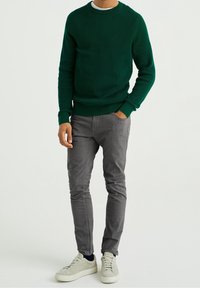 Groene geribbelde trui, grijze slim-fit broek en lichtgekleurde sneakers. Eenvoudig ontwerp met ronde hals en textuurstof.